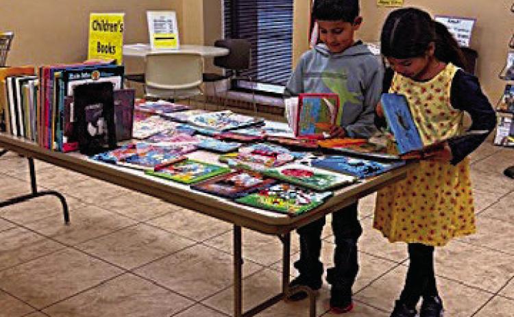 Siblings Andre and Ava Oltivero look at some of the children's books featured at this week's annual book sale at Rhoads Memorial Library. Fiction and non-fiction books are offered, too, along with movies, audio books, music CDs, and more.